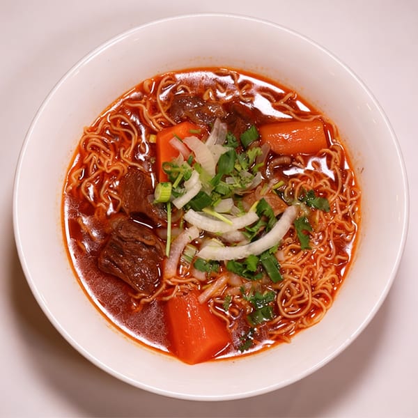 A bowl of Saigon Pho's Vietnamese beef stew with noodles, carrots, and herbs.