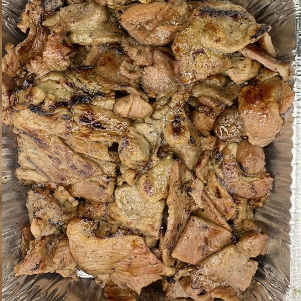 Close-up of grilled Vietnamese pork slices with char marks in a foil container.