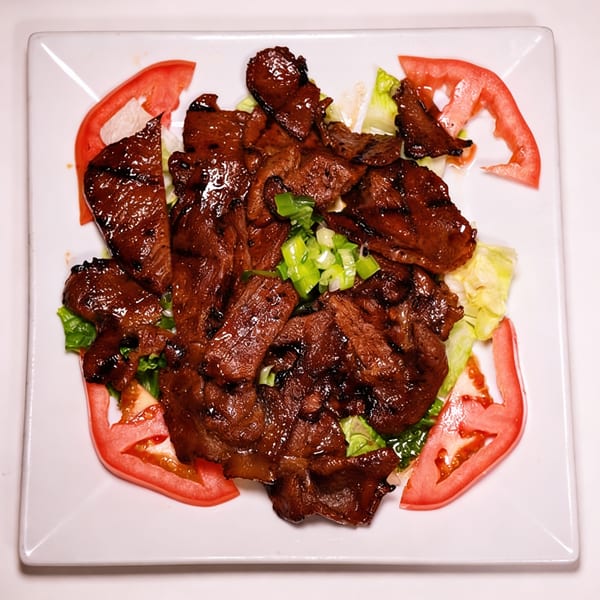 Saigon Pho's grilled beef with lettuce, sliced tomatoes, and green onions on a white plate.