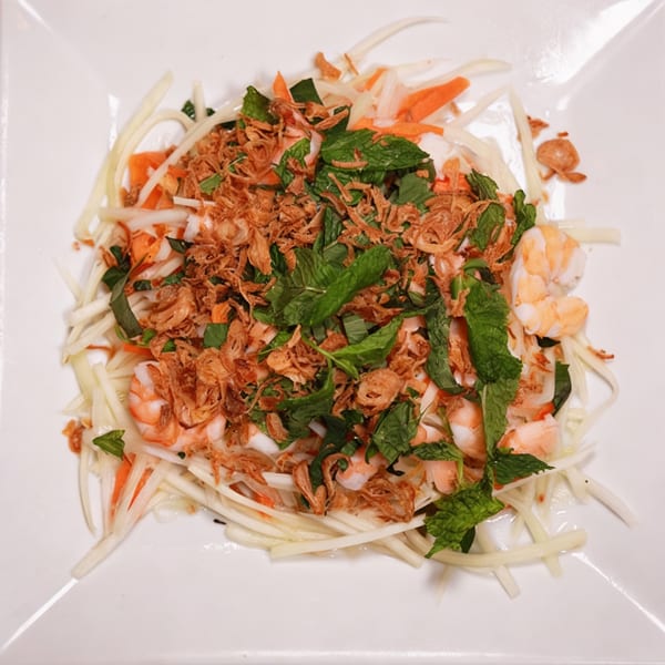 Vietnamese papaya salad with shrimp, mint, and crispy fried shallots on a white plate.