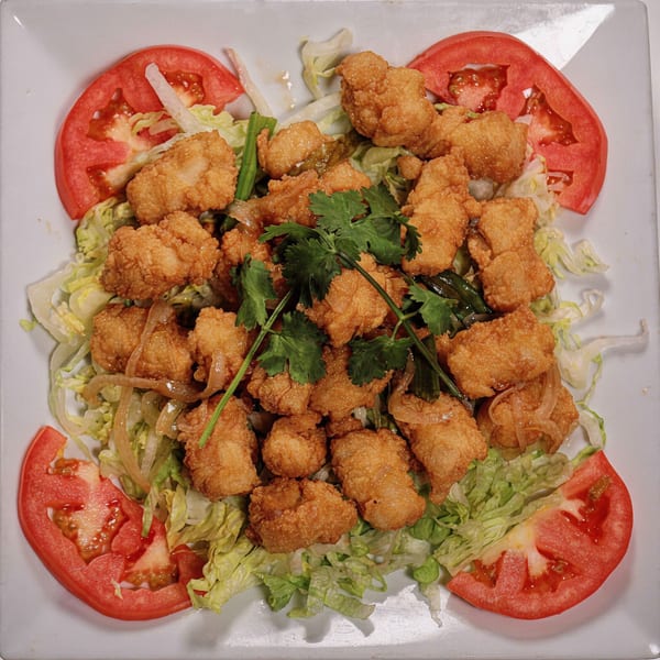 Crispy fried chicken or fish pieces on a bed of lettuce with tomato slices and cilantro garnish.