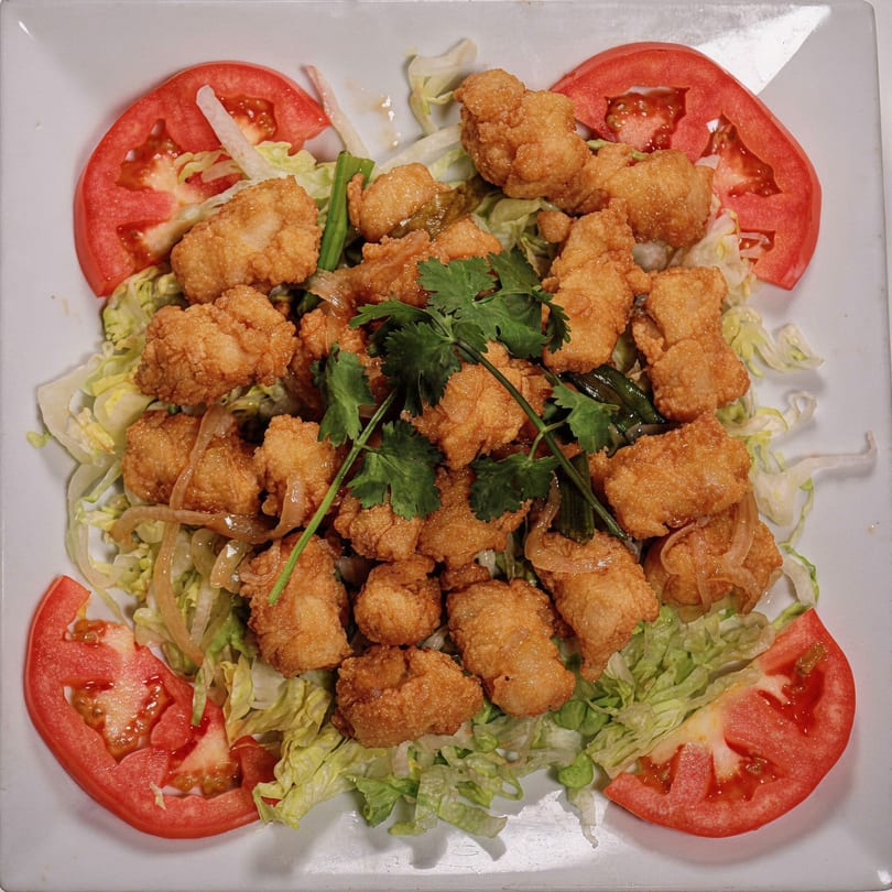 Crispy fried chicken or fish pieces on a bed of lettuce with tomato slices and cilantro garnish.