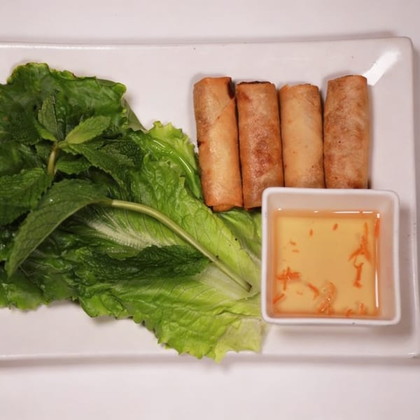 Four crispy Vietnamese spring rolls with fresh lettuce, mint, and a side of dipping sauce.