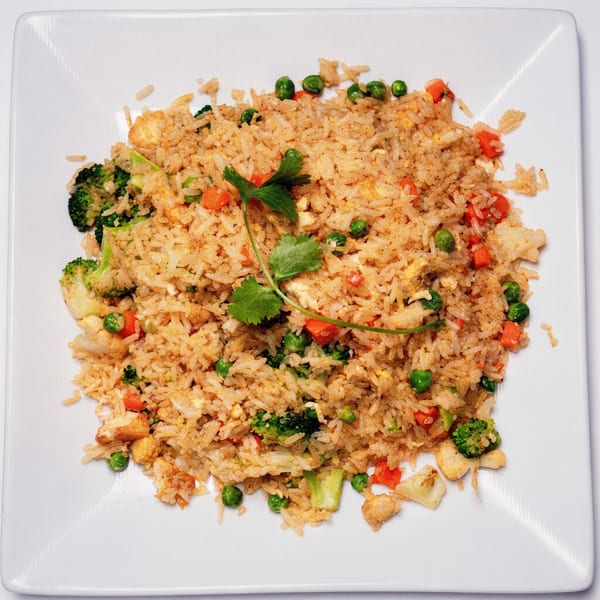 A plate of Vietnamese fried rice with chicken, broccoli, peas, and carrots, garnished with cilantro.